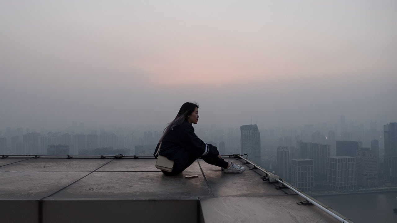 A photo of a woman sitting down on the edge of a city building rooftop pondering on the difference between Legal Separation, Annulment or Declaration of Nullity of Marriage