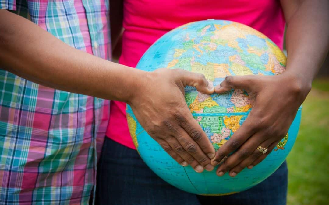 Two people holding a globe while forming a heart with their hands to symbolize adoption of a Filipino child in another country