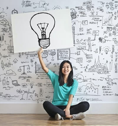 A woman sitting on the floor holding a big card with light bulb drawing