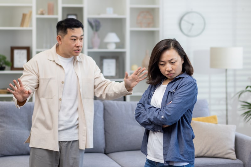 Family quarrel, asian couple man and woman yelling at each other, family conflict, asians at home standing angry in living room