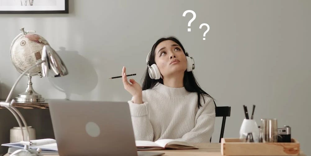 A woman in front of her computer thinking deeply with two floating question marks
