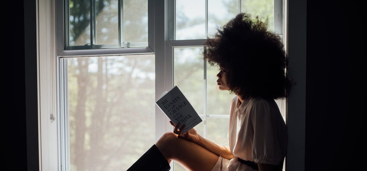 A woman sitting on a window while reading a book