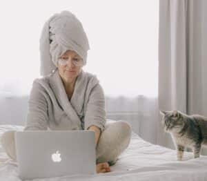 A legitimate spouse using her lapton on a bed beside her cat
