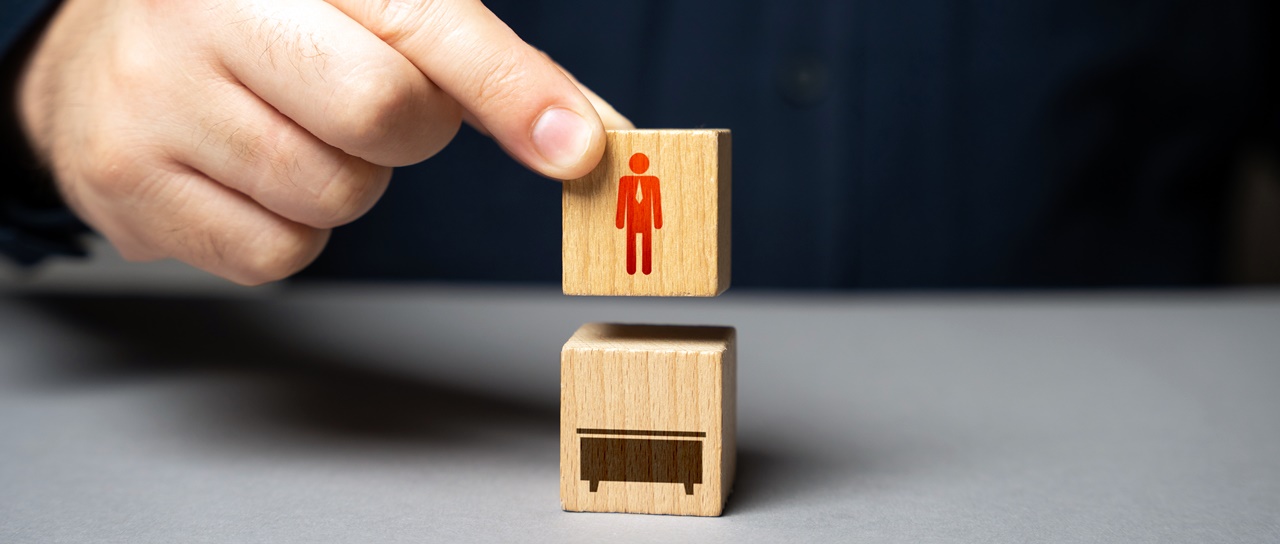 A person about to put a wooden block with a human drawing inside another wooden box