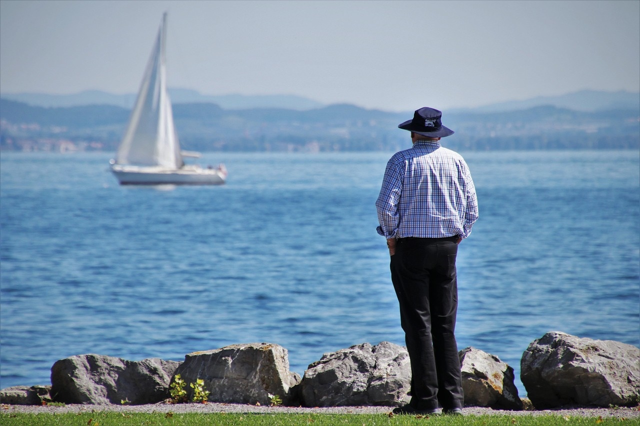 An old man looking at a sailing boat